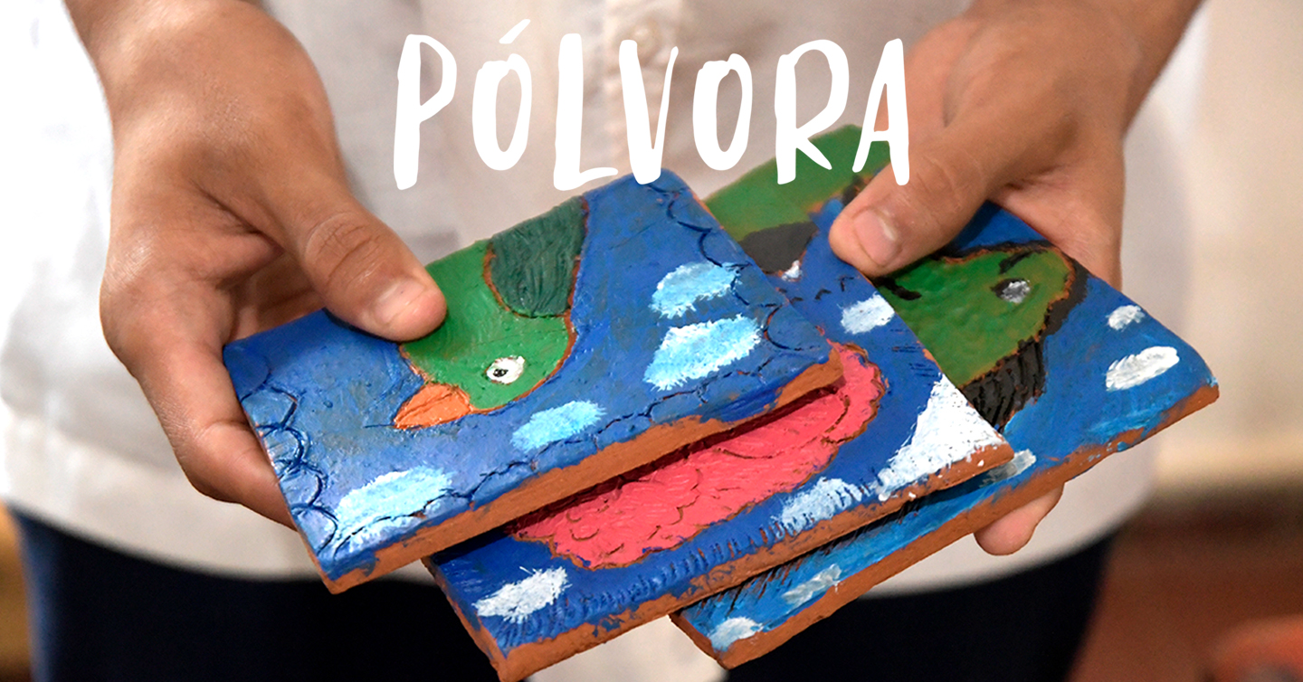 Unas manos con tres azulejos de barro pintados con animales o paisajes y el texto Pólvora