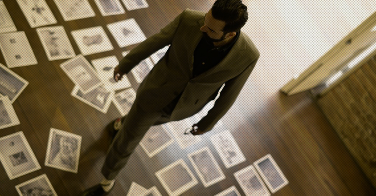 La fotografía muestra a un hombre, visto desde arriba, que camina entre fotografías que están en el suelo.