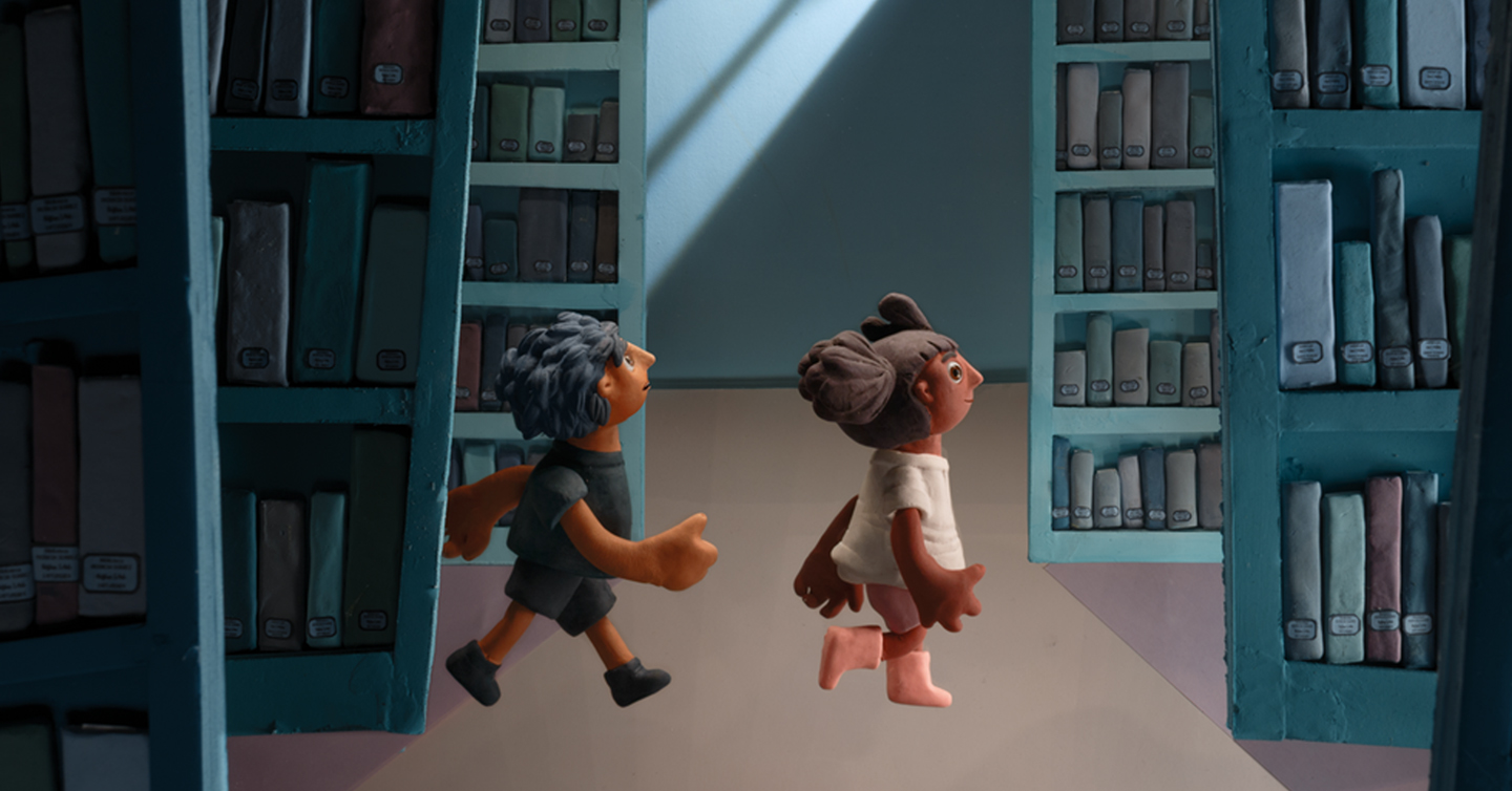 Fotograma de una de las animaciones. Una niña y un niño hechos con plastilina caminan entre las estanterías de una biblioteca.