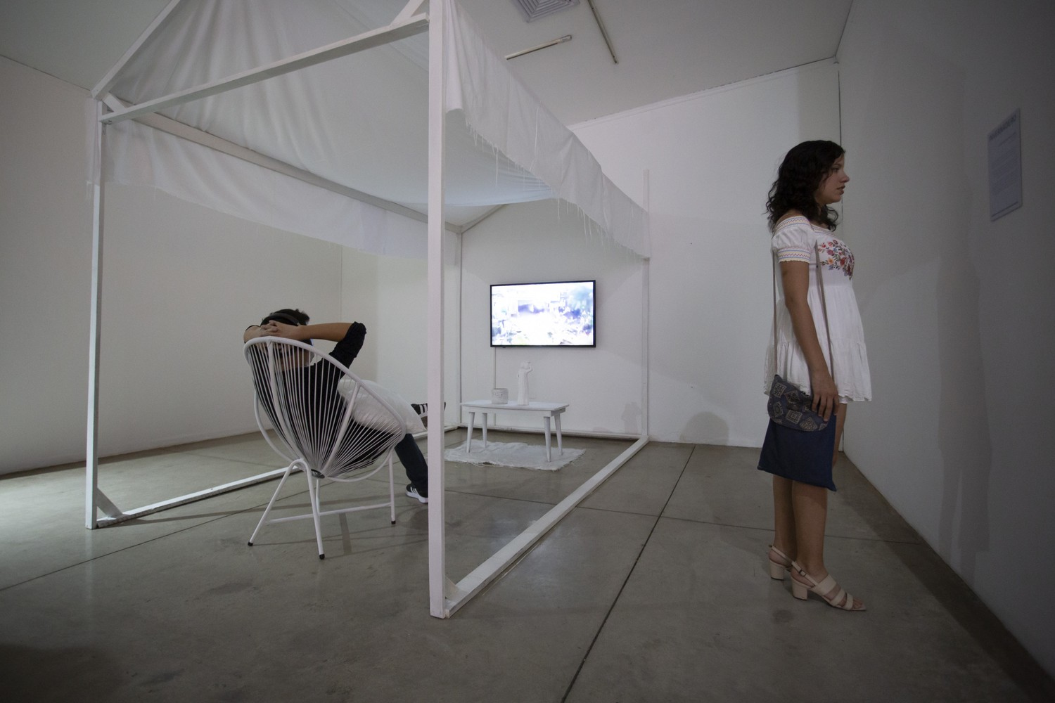 Mujer mirando obra y hombre sentado en una silla mirando pantalla de televisión