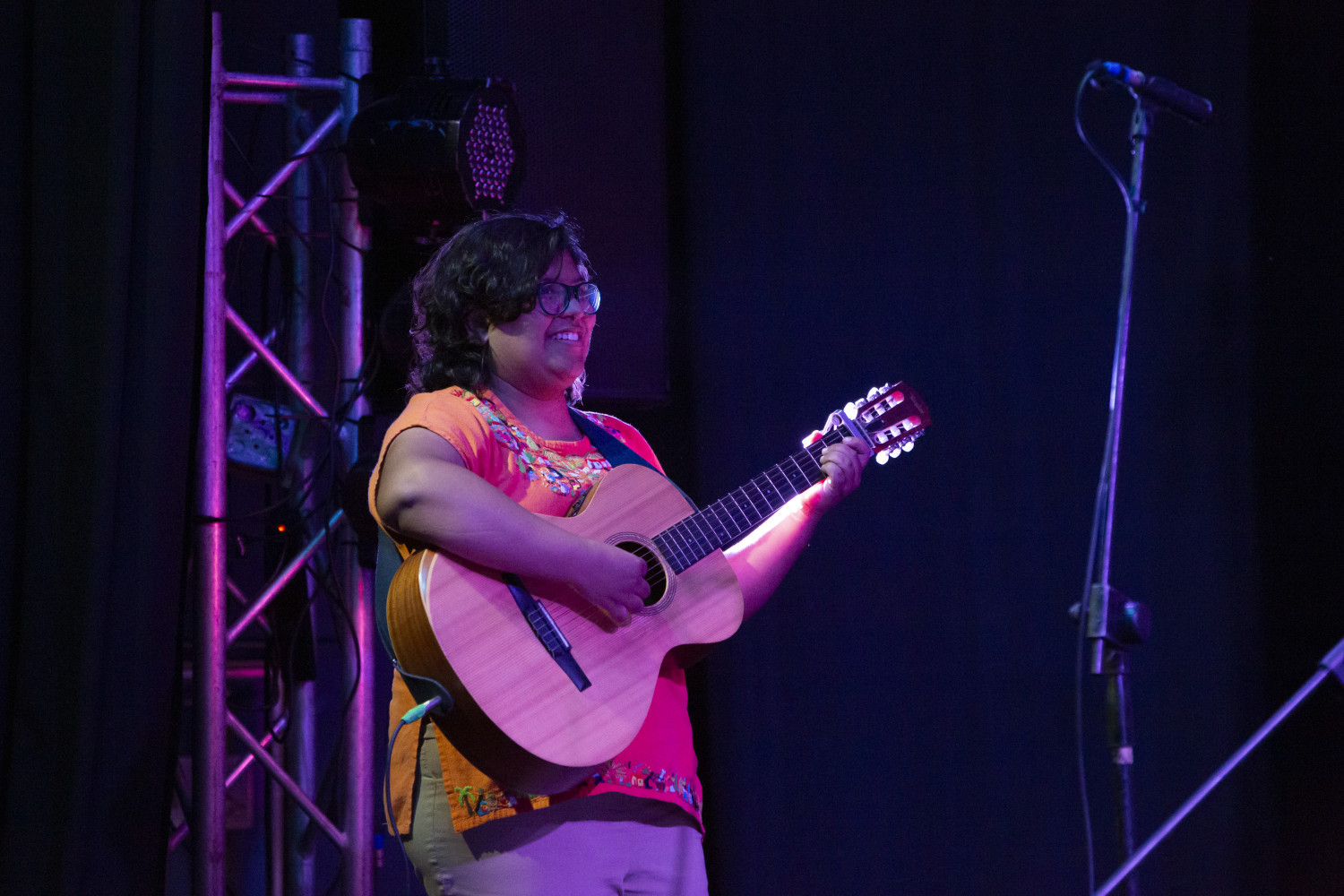 Mujer sonriendo sobre el escenario, tocando la guitarra